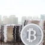 A collection of bitcoin and coins rests on a wooden table, with a cityscape visible in the background.