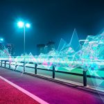 A vibrant city street illuminated by neon lights and a row of glowing lights, creating a lively nighttime atmosphere.