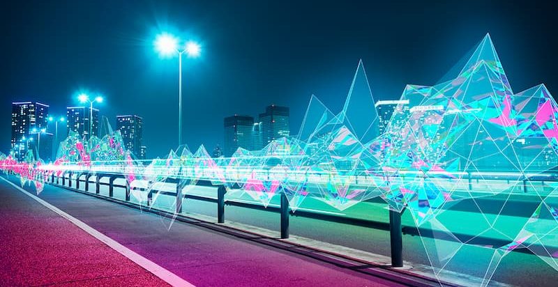 A vibrant city street illuminated by neon lights and a row of glowing lights, creating a lively nighttime atmosphere.