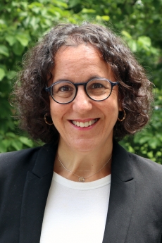 A professional woman wearing glasses and a black blazer, smiling warmly.